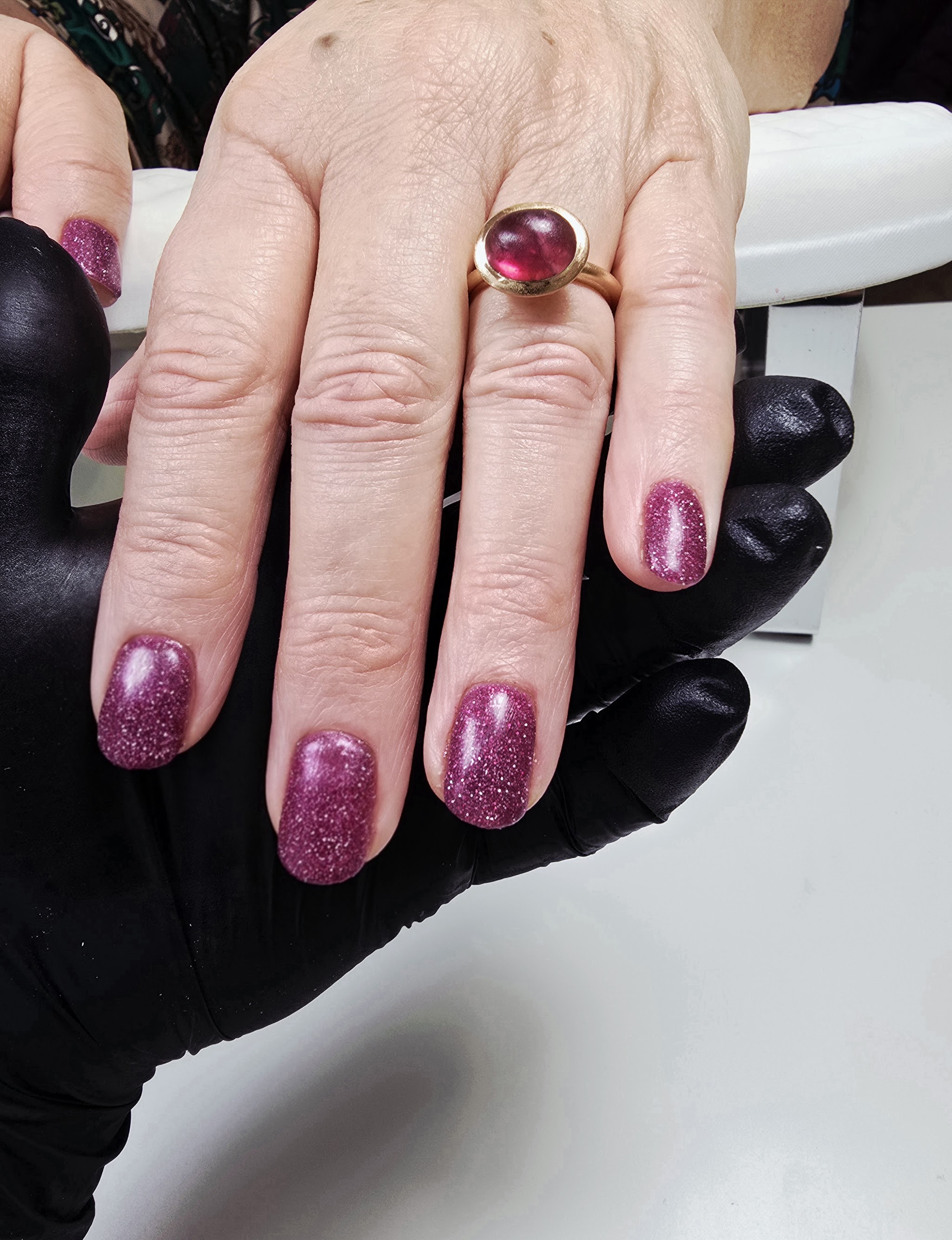 Magenta glitternagels op een hand met een ring met roze steen