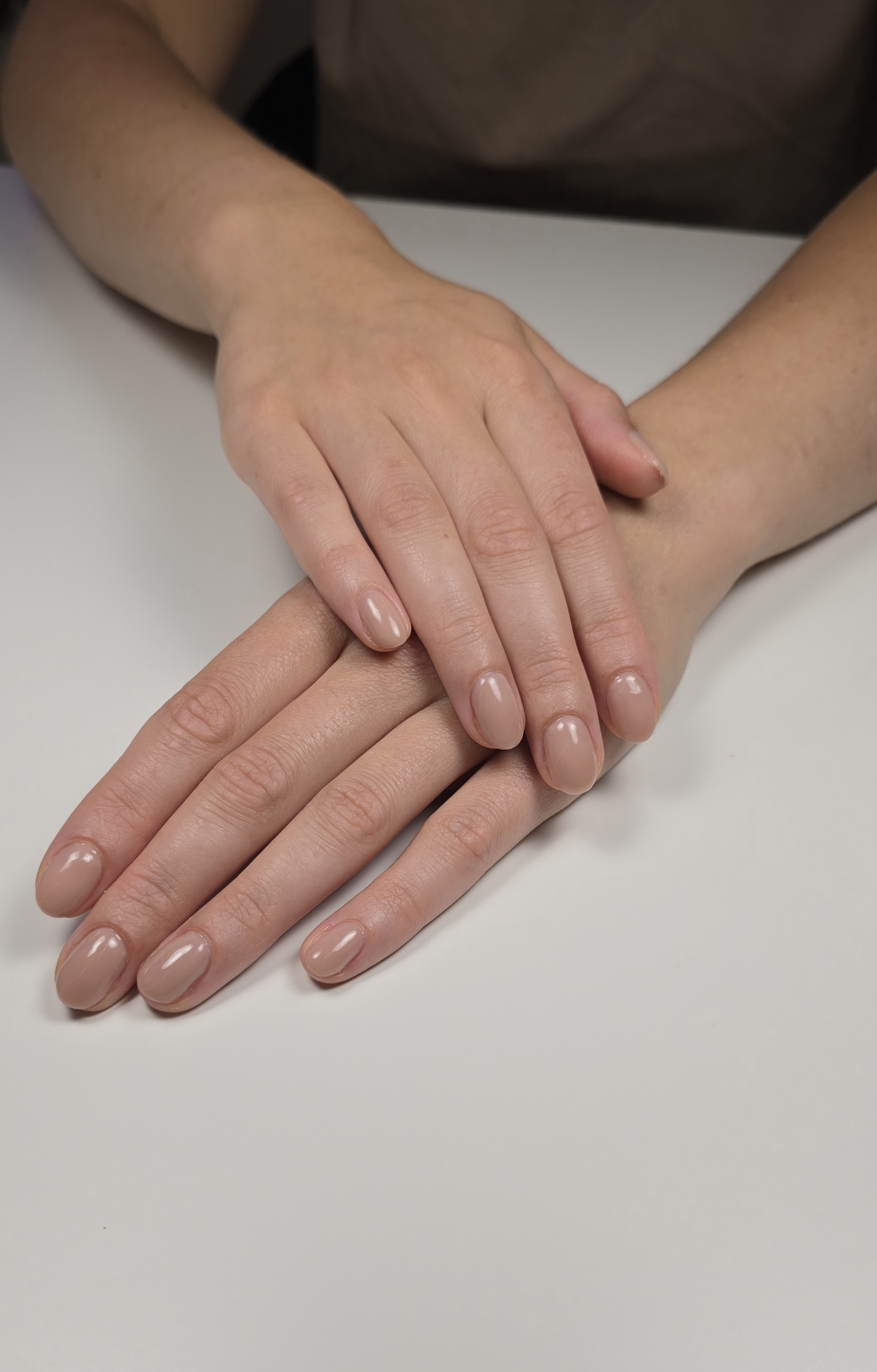 Verzorgde naturel nagels, twee handen over elkaar op een witte tafel