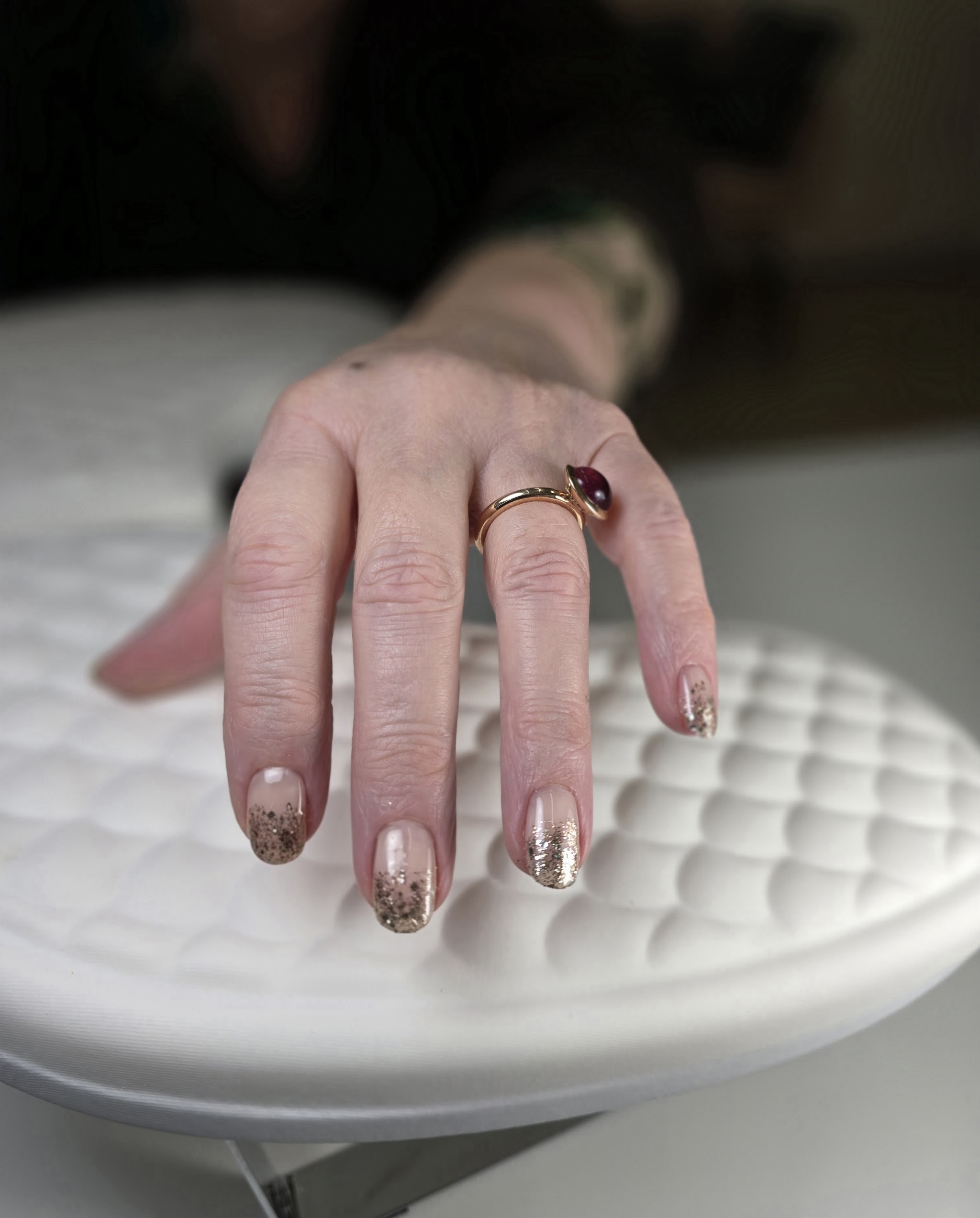 Nude nagels met gouden glitter op de punten, de hand rust op het witte handkussen