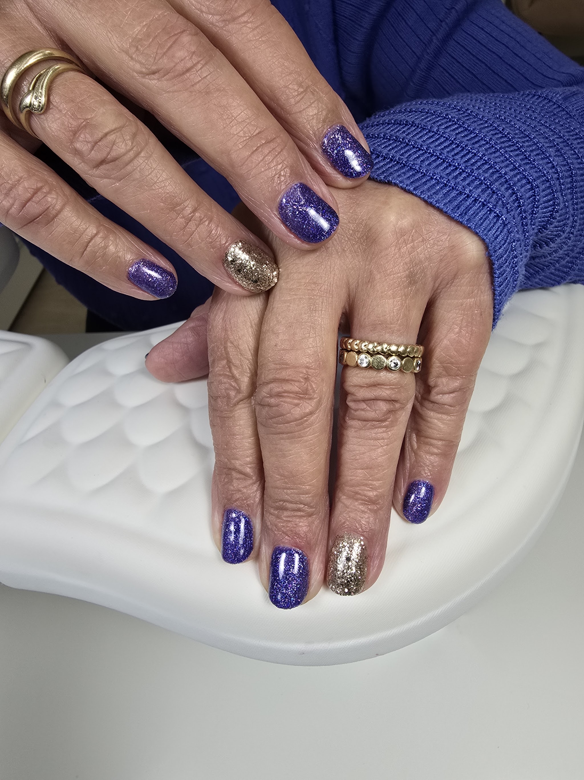 Paarse glitternagels met een gouden accentnagel op het handkussen