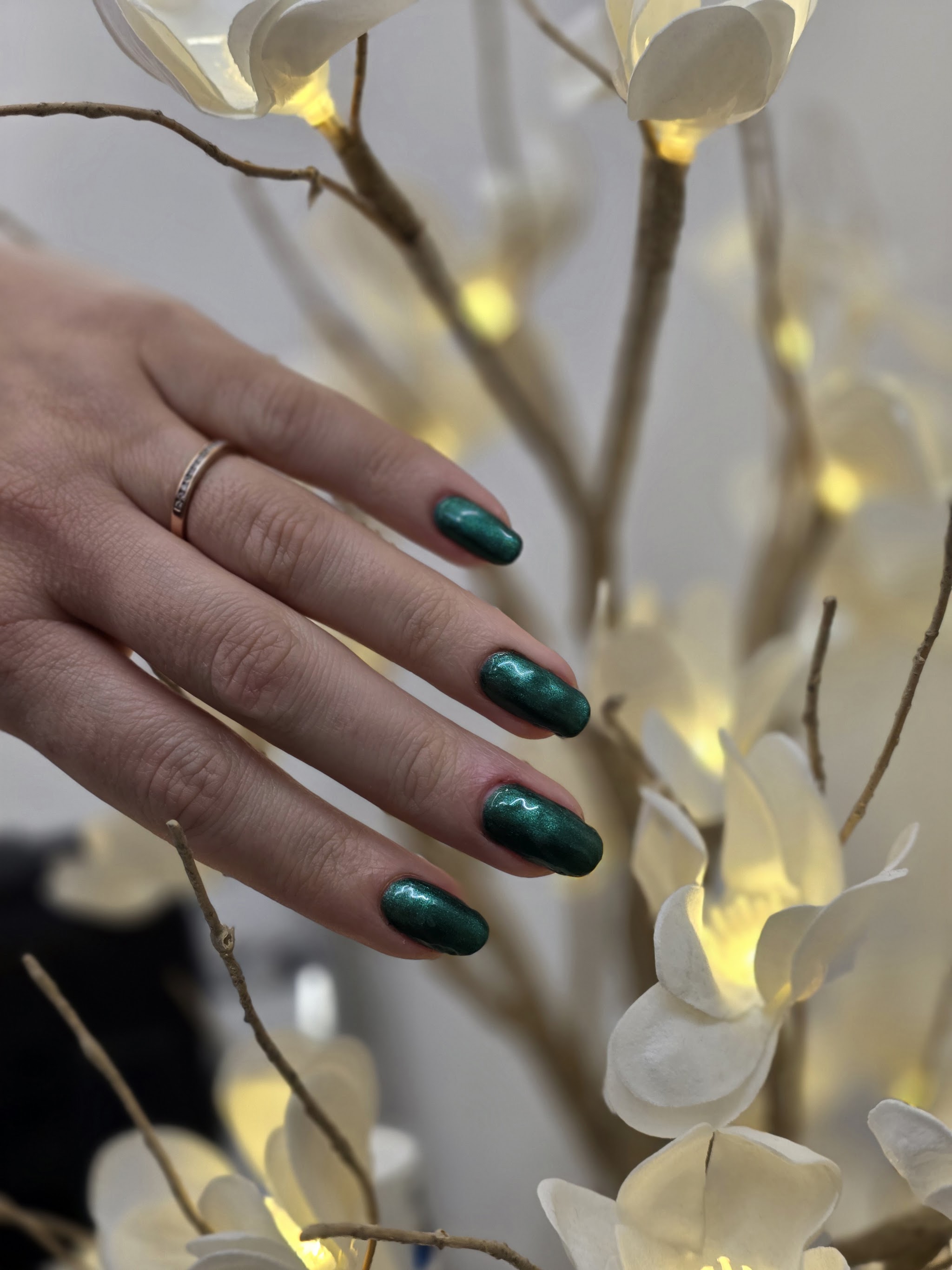 Donkergroene nagels naast een tak met witte bloemen en lampjes